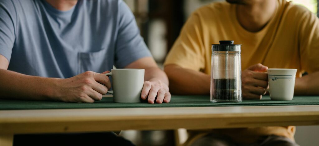 Two friends enjoy coffee together at a wooden table indoors, fostering connection.